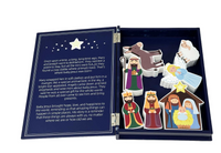 An open Bible story board book with a navy blue cover and interior, showing printed text on one side and colorful illustrated cutout figures on the other, including a bear, wise men, shepherds, and baby Jesus in a stable.